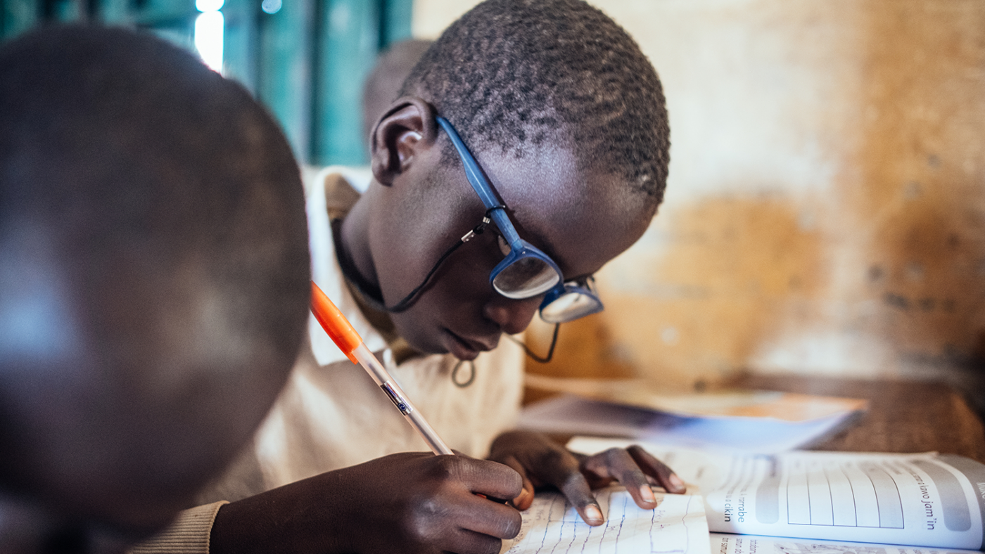 A child wearing glasses writes in a notepad.