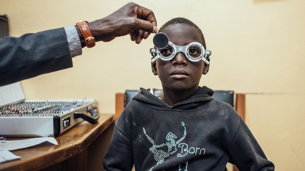 A child has his eyes examined with trial lenses.