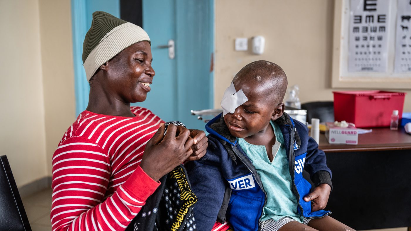 Chancy sits on his mother's lap with a bandage over his right eye.