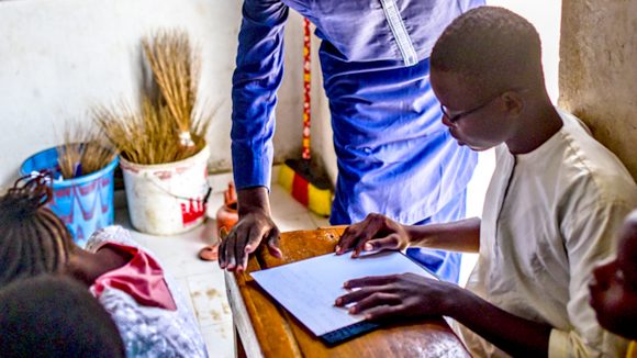 A student in Senegal reads braille in the classroom as a teacher looks on.