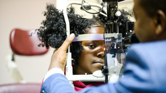 A girl sits at a clinical machine during an eye test.