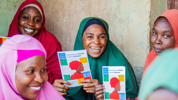 A group of smiling women in Nigeria hold posters and leaflets about family planning.