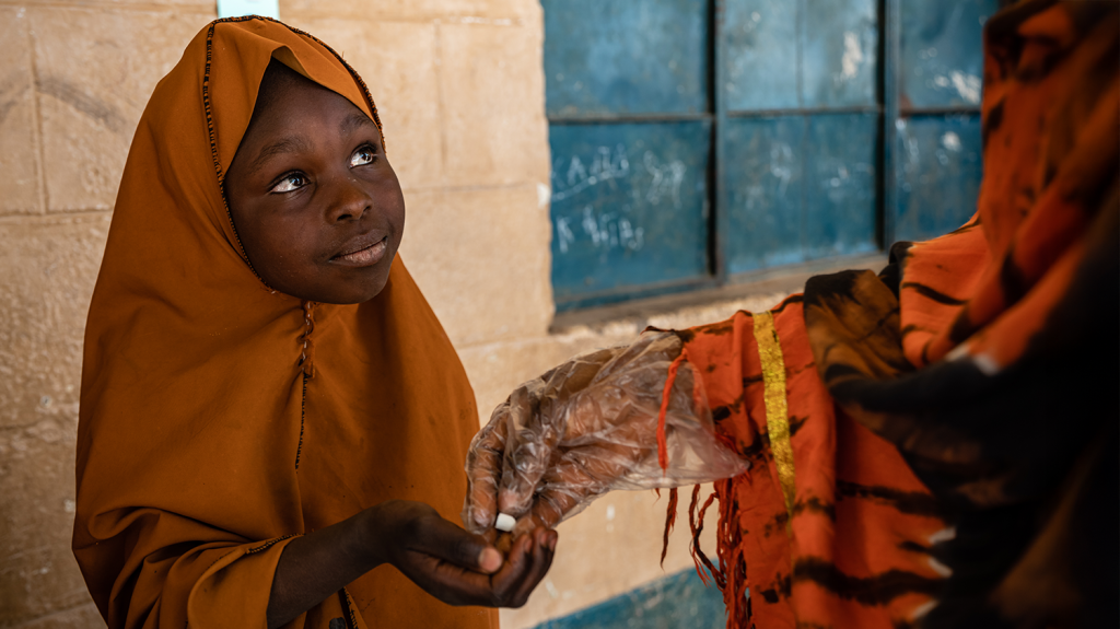 A tablet is placed in the palm of a smiling little girl who's wearing an orange headscarf.