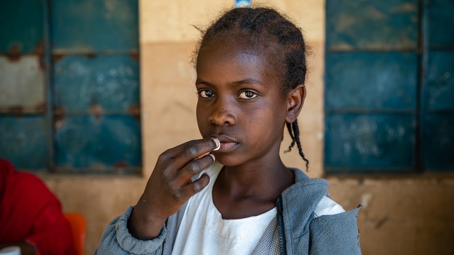 A young girl puts a tablet to her mouth.