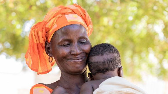 A woman wearing a headscarf holds a baby to her chest.