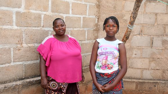 A girl wearing a red pair of glasses stands with a woman outside.