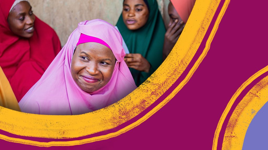 A woman wearing a pink chador smiles while looking away from the camera.