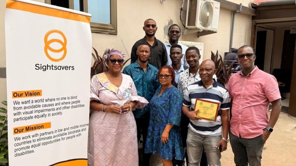 The Sightsavers Sierra Leone country team pose for a group photo next to a Sightsavers banner.