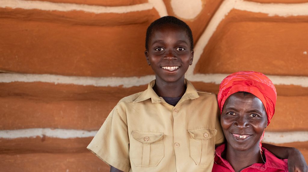 A boy stands next to his mother. His hand is resting on her shoulder.