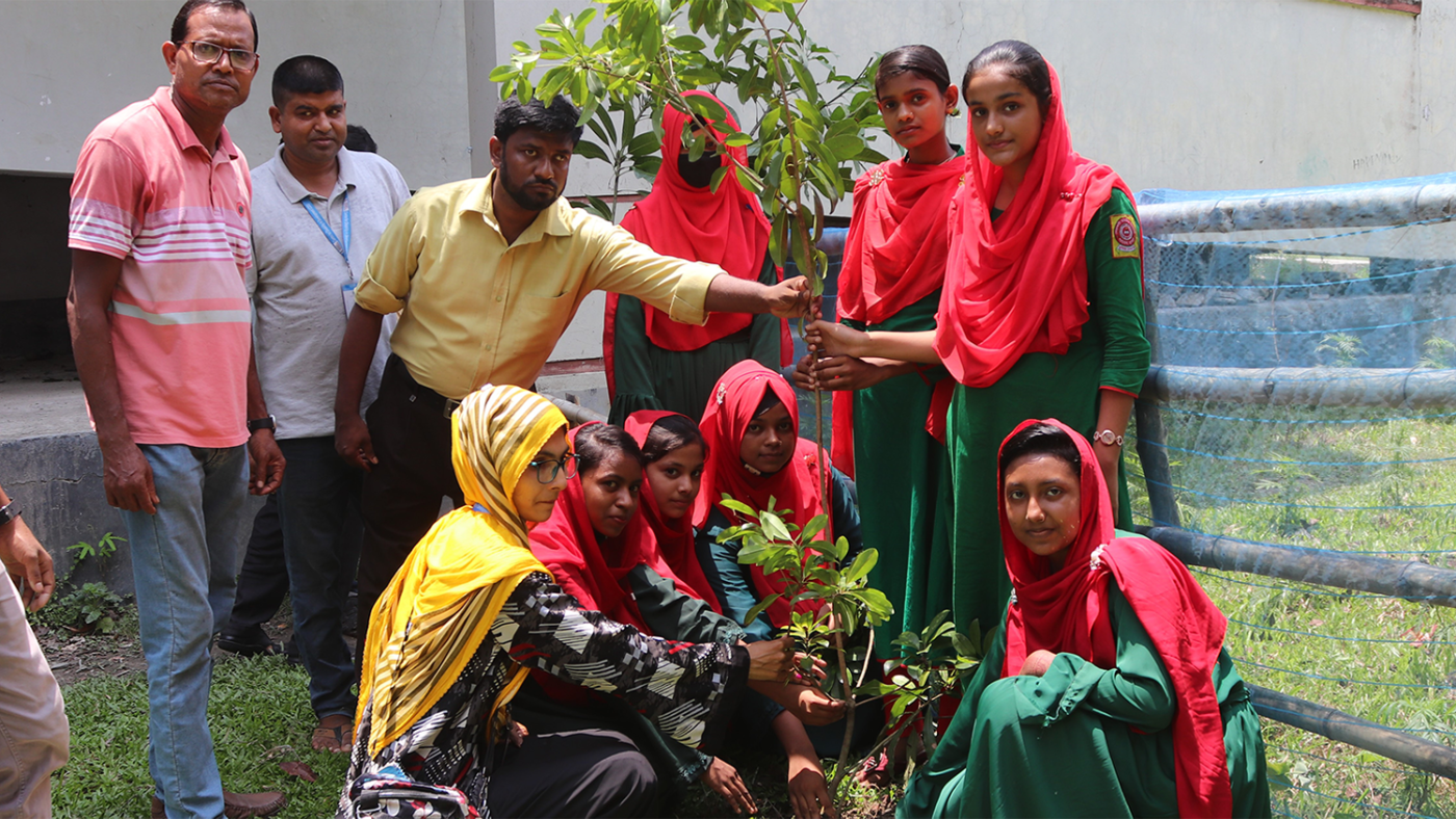 A group of adults and students in colourful clothing gather around two trees.