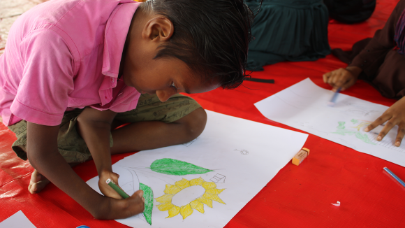 A little boy with a limb impairment concentrates on drawing a sunflower.