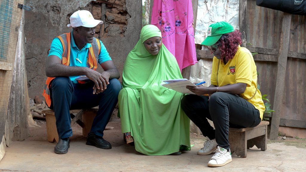 A woman holding a clipboard collects information from a woman wearing a chador.