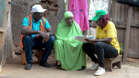 A woman holding a clipboard collects information from a woman wearing a chador.
