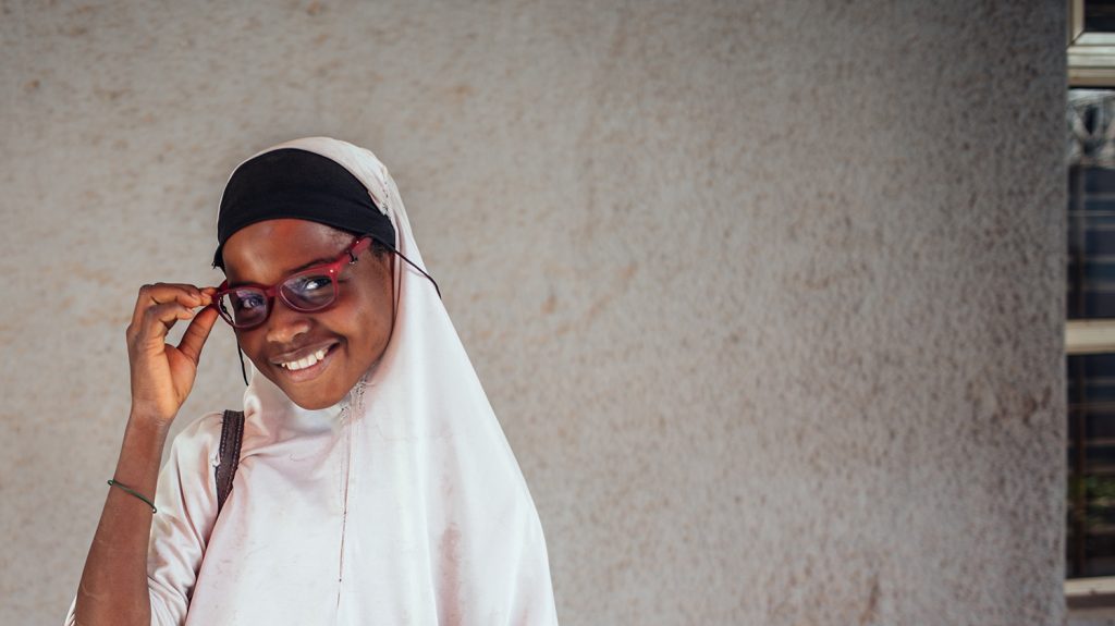 A girl wearing a white headscarf smiles while adjusting a pair of red glasses.