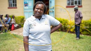 A smiling woman wearing a Sightsavers T-shirt stands with her hand on her hip.