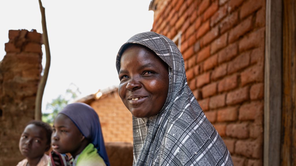 Ruth, who is wearing a head scarf, sits in front of a brick wall. Two of her children are sitting next to her.
