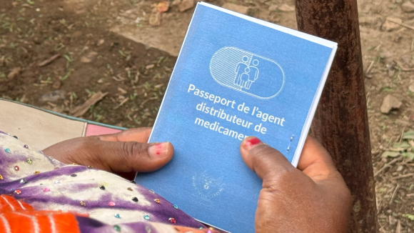A woman holds a copy of the CDD passport. The title in French reads: 'drug distributor's passport'.