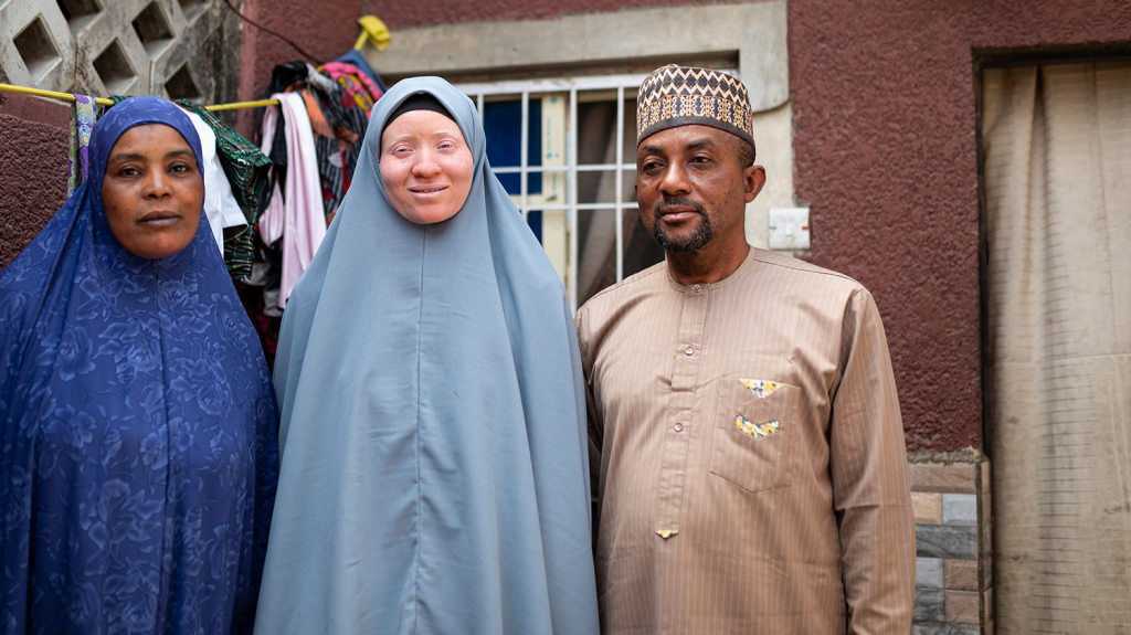 Saudat stands in the middle of her parents, in front of a house with a washing line.