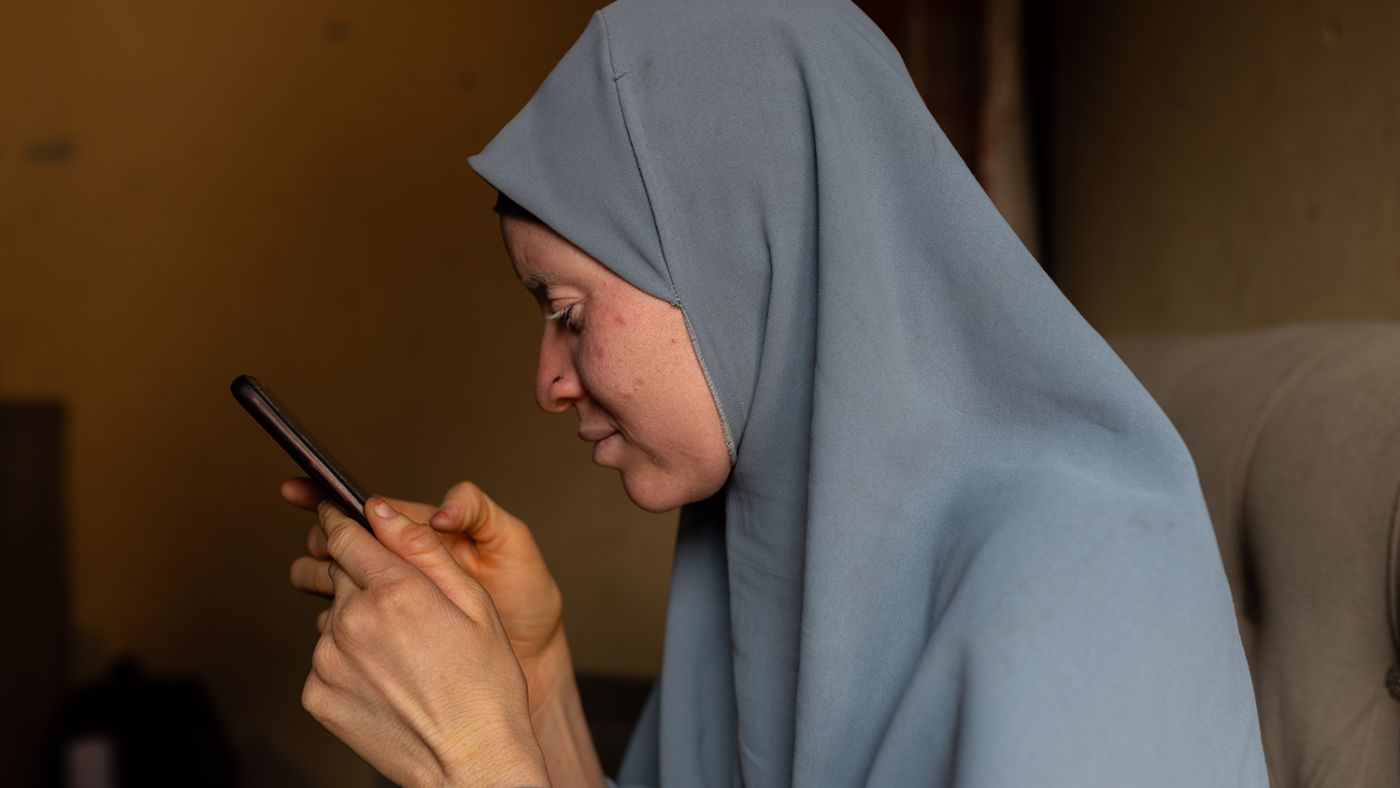 Saudat, wearing a grey hijab, is typing on a mobile phone.